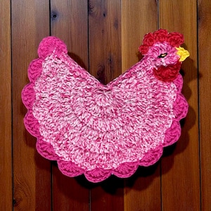 Pode incluir: Um suporte de panela de croch&ecirc; em forma de galinha com corpo em fio matizado rosa e branco e borda festonada. A cabe&ccedil;a possui crista e barbelas vermelho-brilhantes, bico amarelo e um olho preto, feito com um padr&atilde;o de pontos texturizados.