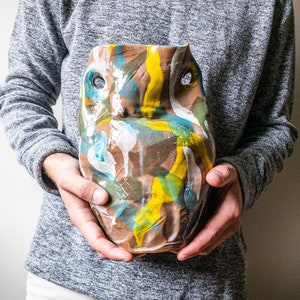 以下が含まれることがあります： 手作りのセラミック製のフクロウ型花瓶で、表面はテクスチャード加工されています。花瓶は茶色のベースで、黄色、青、白、緑のカラフルな抽象的な筆致が特徴です。フクロウには2つの目の穴があり、ユニークで芸術的なデザインです。