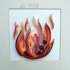Pode incluir: Uma obra de arte em quilling emoldurada que retrata uma chama estilizada. A obra de arte usa tiras de papel vermelho, laranja e amarelo para criar a forma do fogo. A palavra "FIRE" est&aacute; escrita acima da chama.