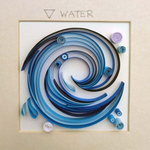 Pode incluir: Uma obra de arte em quilling emoldurada que retrata uma onda estilizada em tons de azul, com a palavra "WATER" acima. A obra apresenta tiras de papel enroladas dispostas em um padr&atilde;o espiral, com pequenos detalhes de papel enrolado em branco e roxo.