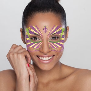 May include: A woman with a purple, yellow, and green face mask with a fleur-de-lis design. The mask is a decorative face sticker.