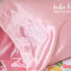 May include: A pink satin pillowcase with white embroidered initials "A.M.C." and the text "Sadie & Bean HAND CRAFTED ACCESSORIES".
