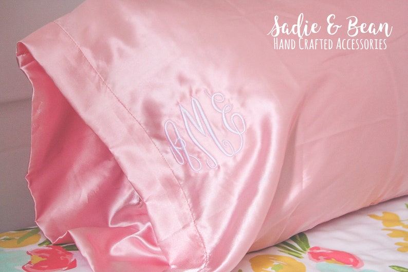 May include: A pink satin pillowcase with white embroidered initials "A.M.C." and the text "Sadie & Bean HAND CRAFTED ACCESSORIES".