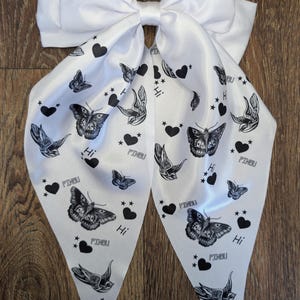 May include: A white satin hair bow with a large bow and long, pointed tails. The tails are decorated with black butterfly and swallow illustrations, hearts, stars, and the word "Hi".