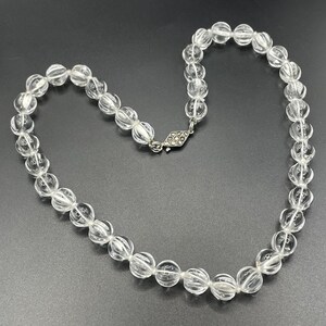 May include: A clear crystal beaded necklace with a silver clasp. The beads are faceted and have a slightly rounded shape.
