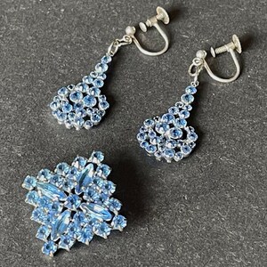 Könnte beinhalten: Ein Set vintage Ohrclips und eine Brosche mit einem Cluster aus hellblauen Strasssteinen in einem geometrischen Design.