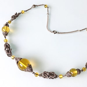 Puede incluir: Un collar de cadena de plata con un cierre de plata y cuentas de vidrio amarillo. Las cuentas están engastadas en filigrana de plata.