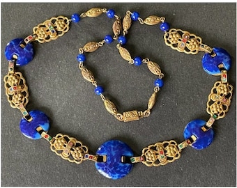 Puede incluir: Un collar de oro con piedras azules y multicolores. El collar tiene un diseño decorativo con un motivo floral. El collar está hecho de metal y tiene un cierre de broche.