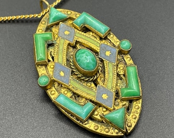 Op de afbeelding: Goudkleurige hangerketting met een ovale hanger. De hanger heeft groene en blauwe geometrische vormen en een centrale ovale groene steen. De ketting heeft een fijne gouden ketting.