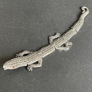 May include: A silver lizard bracelet with red rhinestone accents. The bracelet is made of small, round stones that are set in a silver metal.
