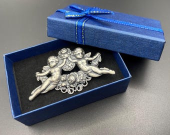 Possivelmente um broche vintage Askew London antigo, em formato de querubim e cupido, com detalhes florais e acabamento em prata antiga.