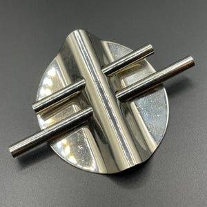 Puede incluir: Un cenicero de metal plateado con base circular y cuatro barras cilíndricas. El cenicero tiene un diseño acanalado en la base y está sobre un fondo oscuro. El cenicero es un artículo decorativo.