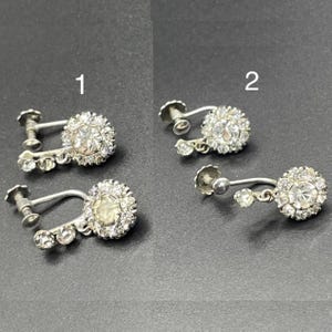May include: Two pairs of silver clip-on earrings with clear rhinestone accents. The earrings are labelled "1" and "2".