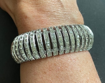 May include: A silver bracelet with a row of clear rhinestones. The bracelet is flexible and has a hinged clasp.