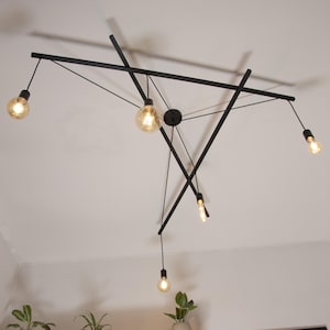 Può includere: Un moderno lampadario da soffitto in metallo nero con cinque lampadine. Il lampadario ha un design geometrico con linee che si incrociano.
