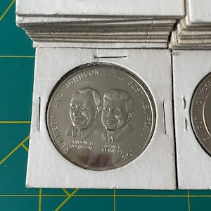 May include: A silver coin with the text "KENNEDY AND JOHNSON... THE BEST MEN FOR THE JOB" and portraits of Lyndon B. Johnson and John F. Kennedy.