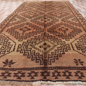 Pode incluir: Um tapete retangular, tecido à mão, com um padrão geométrico em tons de castanho e bege. O tapete apresenta um design central em forma de diamante e detalhes de borda intrincados. O tapete tem uma borda com franjas.