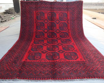 May include: A large, rectangular red rug with a dark border and intricate geometric patterns. The central design features repeating dark blue octagonal shapes. The rug has a fringed edge and appears to be made of woven material.