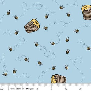 May include: Light blue fabric with a repeating pattern of cartoon bees and beehives. The bees are yellow and black, and the beehives are brown and yellow. Dotted lines suggest the bees' flight paths. The fabric is from Riley Blake Designs.