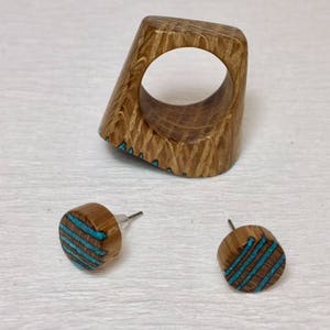 Puede incluir: Un anillo de madera y un par de pendientes con incrustaciones de turquesa. El anillo es una banda gruesa con forma cuadrada y un gran agujero en el centro. Los pendientes son redondos y tienen un patr&oacute;n de rayas turquesa.