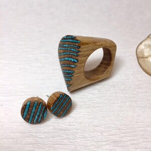 Puede incluir: Un anillo de madera y un par de pendientes con incrustaciones de turquesa. El anillo tiene forma de l&aacute;grima y los pendientes son redondos. La madera es de color marr&oacute;n claro y las incrustaciones de turquesa son de un azul brillante.