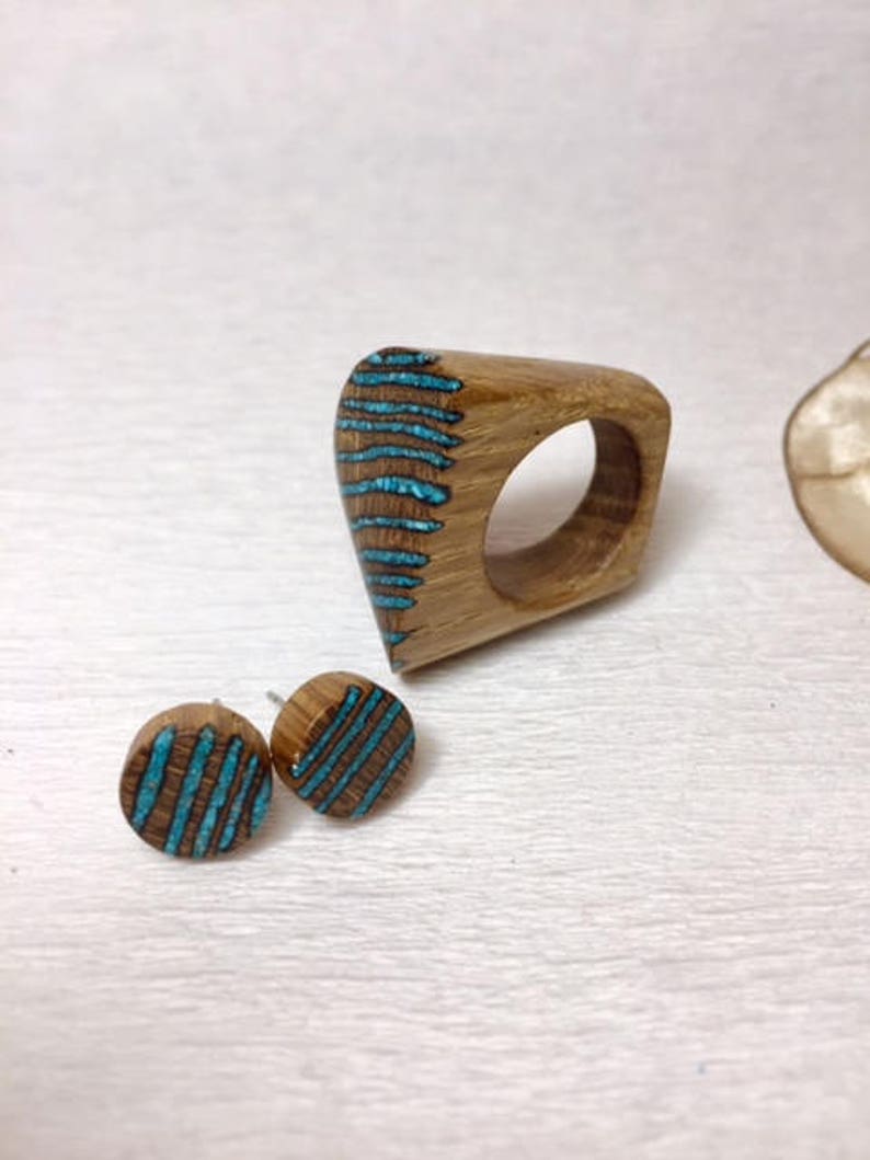 Puede incluir: Un anillo de madera y un par de pendientes con incrustaciones de turquesa. El anillo tiene forma de l&aacute;grima y los pendientes son redondos. La madera es de color marr&oacute;n claro y las incrustaciones de turquesa son de un azul brillante.