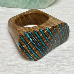 Puede incluir: Un anillo de madera con un dise&ntilde;o de incrustaciones de turquesa. El anillo est&aacute; hecho de madera oscura y tiene un patr&oacute;n &uacute;nico a rayas.