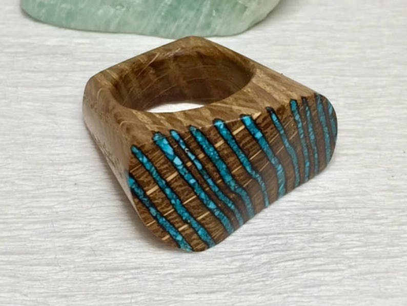 Puede incluir: Un anillo de madera con un dise&ntilde;o de incrustaciones de turquesa. El anillo est&aacute; hecho de madera oscura y tiene un patr&oacute;n &uacute;nico a rayas.