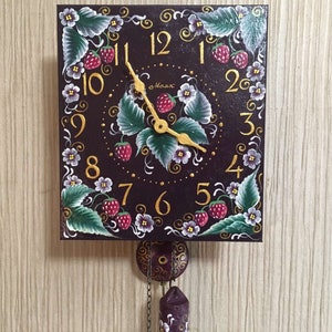 May include: A hand-painted wooden clock with a black face and gold numbers. The clock is decorated with painted strawberries, leaves, and flowers. The clock has a pendulum and is hanging on a wall.