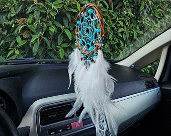 May include: A blue and white dreamcatcher with white feathers hanging from the rearview mirror of a car. The dreamcatcher is made of brown leather and has beads and crystals.