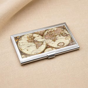 May include: A rectangular metal business card holder featuring a vintage-style world map print on the front cover. The case has a polished silver-tone frame with a hinged opening mechanism and a smooth, metallic finish along the edges and closure.