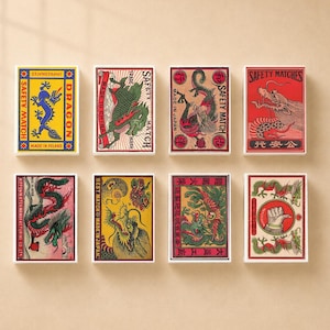May include: A collection of eight rectangular matchboxes arranged in two rows. Each box features distinct, colourful illustrations of dragons and other mythical motifs, with printed text including Safety Match, Made in Japan, and Made in Poland.