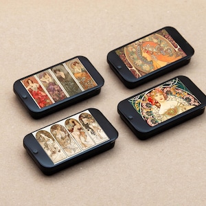 May include: Four black rectangular cases with different Art Nouveau style images of women on the front. The cases are arranged in a row on a light brown surface.
