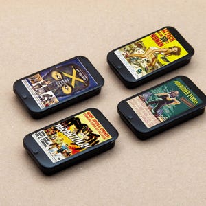 May include: Four black phone cases with different vintage movie posters on them. The posters include "Attack of the 50 Foot Woman", "Forbidden Planet", "Tarantula", and "The X", all in black and white.