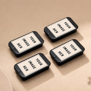 Op de afbeelding: Vier rechthoekige zwarte metalen blikjes met schuifdeksels, elk voorzien van een crèmekleurig label met een dunne zwarte rand en de zwarte tekst "YOUR IMAGE HER" in het midden, gerangschikt in een groep op een lichtbruin oppervlak.