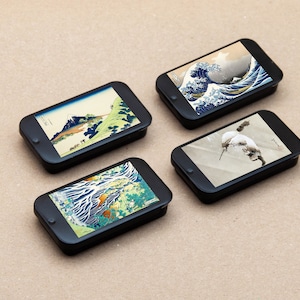 Peut inclure: Quatre étuis rectangulaires noirs avec des estampes japonaises différentes sur le devant. Les estampes comprennent une scène de montagne, une vague, un oiseau et une cascade.