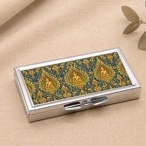 May include: A rectangular silver metal case featuring a top panel with a dark blue background and a repeating gold pattern of seated Buddha figures enclosed in pointed arch shapes, with a metallic latch mechanism on the front edge.