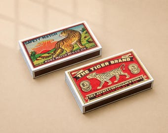 May include: Two rectangular matchboxes featuring vintage tiger illustrations. The top box displays a tiger with a rising sun and the text SAFETY MATCH KOBE MATCH MFG CO LTD. The bottom box shows a tiger with the text THE TIGER BRAND SOLE AGENTS FOR PAPUA NEW GUINEA WM. BRECKWOLDT & CO.