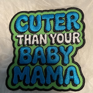 May include: An embroidered patch with a bright green background and a black border. The text CUTER THAN YOUR BABY MAMA is stitched in bold, blue and white lettering. The words are arranged in four lines with a thick, raised, bubble-style font.