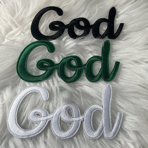 May include: Three embroidered patches featuring the word God in a cursive script font. The top patch is black, the middle patch is dark green, and the bottom patch is white. Each patch has a thick stitched border and a textured fabric surface.