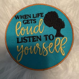May include: A circular embroidered patch with a bright turquoise background and an orange border. It features the black text "WHEN LIFE GETS" and "LISTEN TO" alongside the gold cursive text "loud" and "yourself" with a black silhouette of an afro.