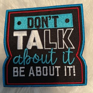 May include: A rectangular embroidered patch with a black background and a blue and red border. The text reads DON'T in black on a blue bar, TALK in white, about it in blue script, and BE ABOUT IT! in white, all featuring detailed stitching.