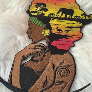 Peut inclure: Un écusson brodé représentant le profil d'une personne à la peau foncée, portant un bandeau vert et une boucle d'oreille dorée. Les cheveux forment le continent africain, rempli d'un paysage de coucher de soleil avec éléphants et flamants.