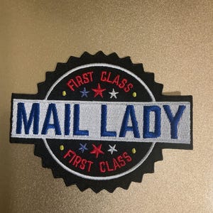 Może przedstawiać: Okrągła haftowana naszywka z czarną ząbkowaną krawędzią, zawierająca napis "FIRST CLASS" w kolorze czerwonym oraz "MAIL LADY" w kolorze niebieskim na białym poziomym pasku. Wzór zawiera małe czerwone, białe i niebieskie gwiazdki oraz żółte kropki.