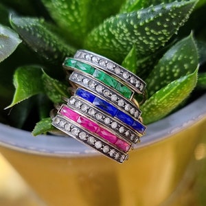 Op de afbeelding: Vijf stapelbare ringen met een rij smaragdgroene, saffierblauwe en robijnrode edelstenen, gezet in een zilveren band met een rij diamanten.