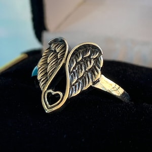 Peut inclure: Une bague dor&eacute;e avec un motif d'ailes d'ange. La bague pr&eacute;sente des textures de plumes d&eacute;taill&eacute;es et une d&eacute;coupe en forme de c&oelig;ur. La bague est pr&eacute;sent&eacute;e dans un &eacute;crin en velours noir.