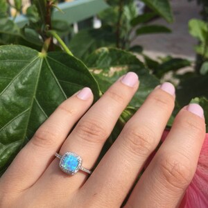 May include: A silver ring with a light blue opal gemstone surrounded by a halo of smaller clear gemstones.
