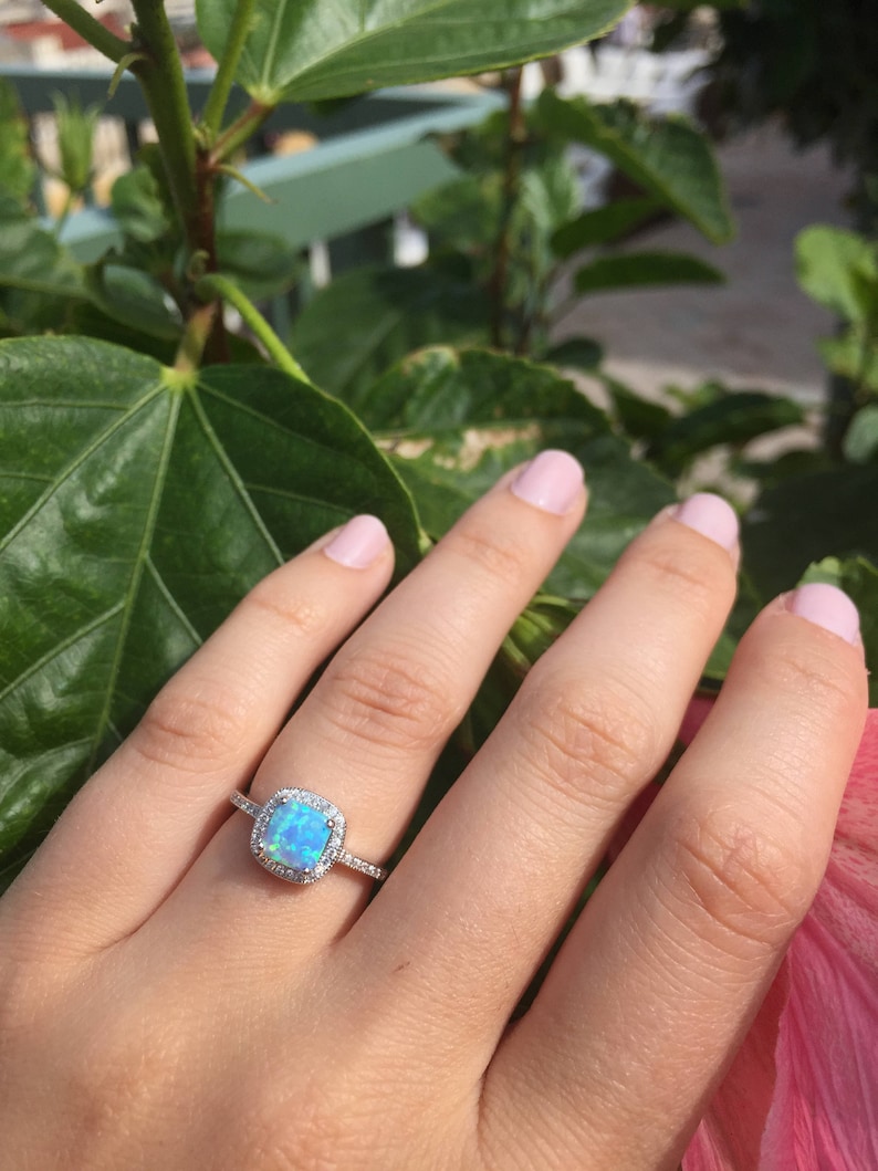 May include: A silver ring with a light blue opal gemstone surrounded by a halo of smaller clear gemstones.