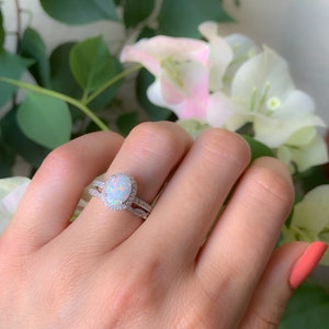 May include: A silver ring set with a large oval opal surrounded by smaller white stones. The ring is on a finger with a light pink nail polish.