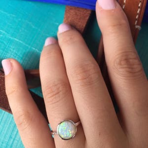 May include: A silver ring with a white opal gemstone. The ring is on a person's finger.